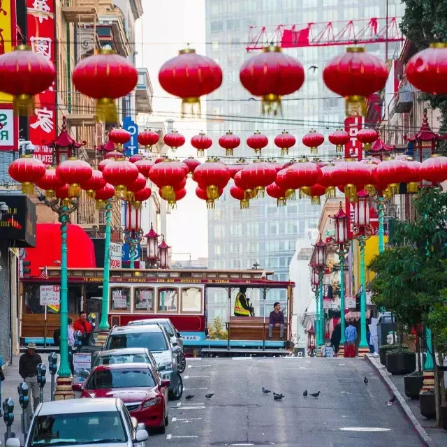 Une rue vallonnée du quartier chinois de San Francisco est représentée avec des lanternes rouges suspendues et un tramway qui passe.